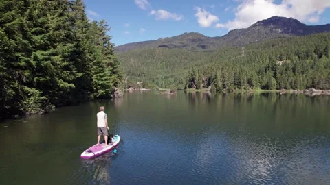 Man paddle boarding on a pristine mountain lake on sunny day with his dog, stand Stock Footage 247646038