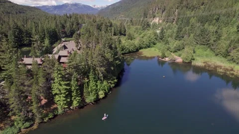 Man paddle boarding on a pristine mountain lake on sunny day with his dog, stand Stock Footage 248214425