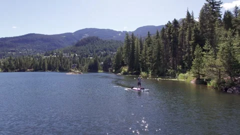 Man paddle boarding on a pristine mountain lake on sunny day with his dog, stand Stock Footage 249728135