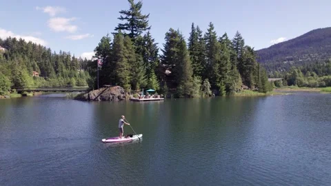 Man paddle boarding on a pristine mountain lake on sunny day with his dog, stand Stock Footage 250951376