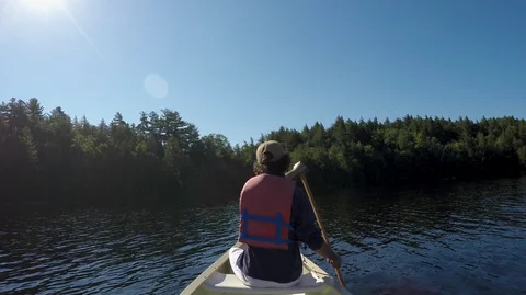 Man paddling a canoe towards the shore of a lake or calm river Stock Footage 90088853