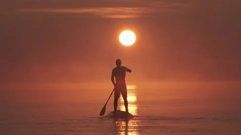 Man paddling on stand up paddle board against background of rising sun. SUP Stock-Footage 244603620