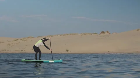Man paddling on stand up paddle board against background of dunes in desert. SUP Stock Footage 244603718