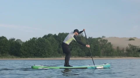 Man paddling on stand up paddle board against background of pine forest and dune Stock Footage 244605730