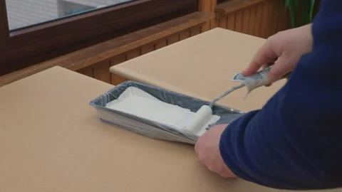 A man, a painter, a carpenter, a hired worker paints a board. Male hands roll Stock Footage 304897842