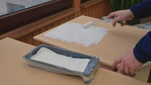 A man, a painter, a carpenter, a hired worker paints a board. Male hands roll Stock Footage 305037899