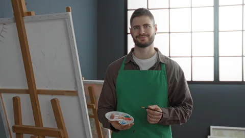 Man painter in green apron holding paint palette and brush at studio easel,.. Stock Footage 337366607