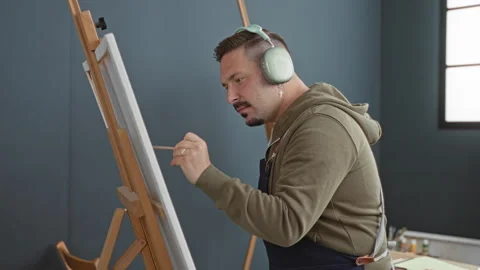 Man painter holds paintbrush to canvas at studio easel, wearing headphones .. Stock Footage 337390581