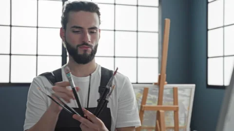 Man painter holds several paintbrushes and selects one with fingers in stud.. Vidéo 337371568
