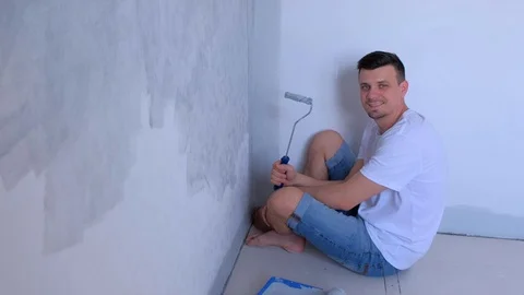 Man painter with paint roller sitting on floor looking at camera and smiling. Stock Footage 123409573