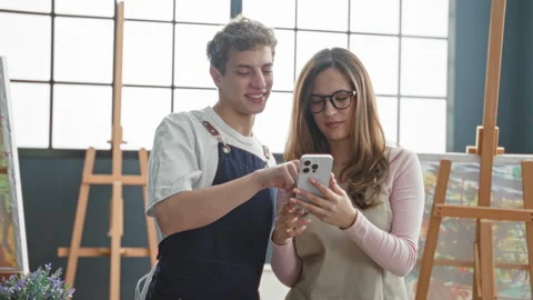 Man painter points finger to smartphone held by woman in studio while both .. Stock Footage 339258319