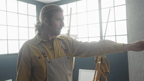 Man painter reaches hand to canvas in art studio with easels and large wind.. Stock Footage 337375456