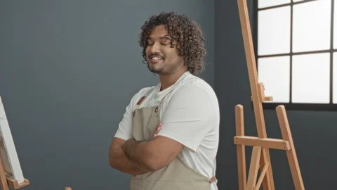 Man painter in studio with arms crossed wearing apron beside wooden easel, .. Stock Footage 337403197