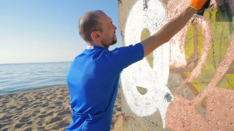 Man painting graffiti on wall on beach Stockbeeldmateriaal 82436595