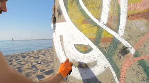 Man painting graffiti on wall on beach 스톡 동영상 82437809