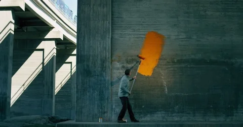 Man painting orange color on grey concrete wall Stock Footage