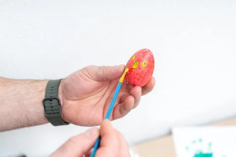 Man painting a red Easter egg with yellow spots at home for the Easter holi.. Photos