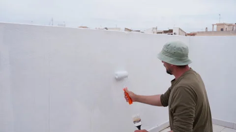 Man painting white wall on rooftop terrace using paint roller for home reno.. Stock Footage 334550208