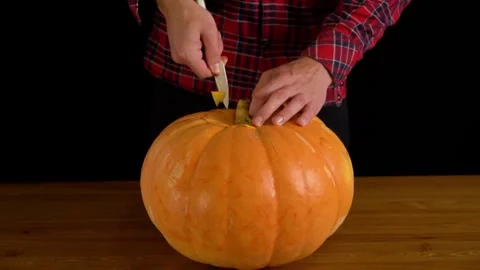 Man paints pumpkin for Halloween while sitting in dark room. Preparing Stock Footage 272459876