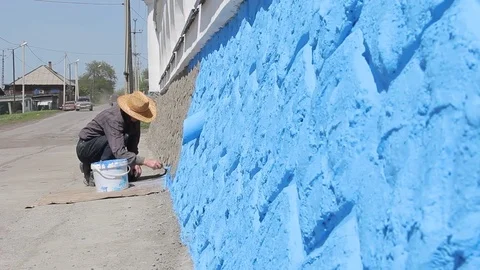 Man paints the wall of the house with blue paint Stockbeeldmateriaal 76141591