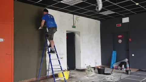 Man paints wall in room during renovation process in a building with simple setu Stock Footage 329437193