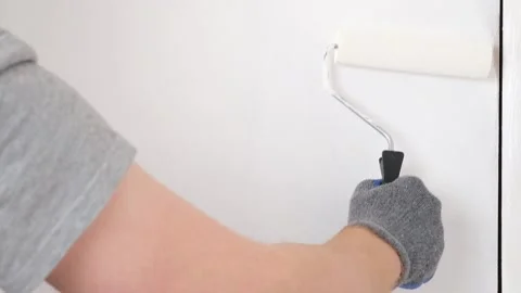 A man paints wooden door white. The painter uses a foam paint roller to apply Stock Footage 211138053