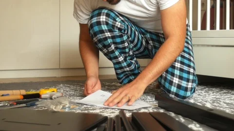 Man in Pajamas Reading Manual Tutorial How to Assemble Wooden Chair 動画素材 97041400