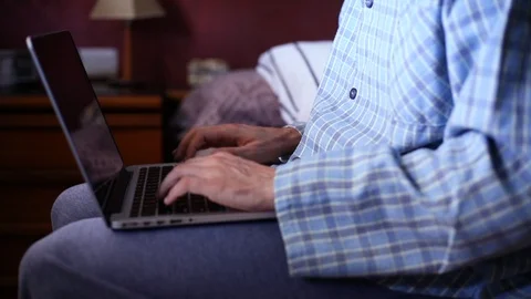 Man in pajamas sitting on the bed is working remotely from home Stock Footage 128961610