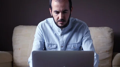 Man in pajamas sitting on the couch is working remotely from home Stock Footage 128967356