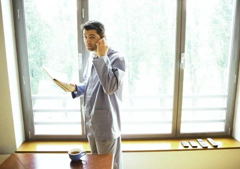 Man in pajamas using cell phone and reading newspaper Foto stock