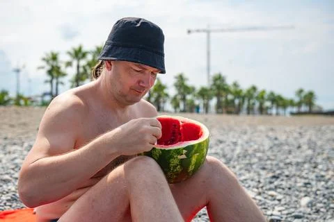 A man in a panama hat eats a watermelon on the beach Stock Photos