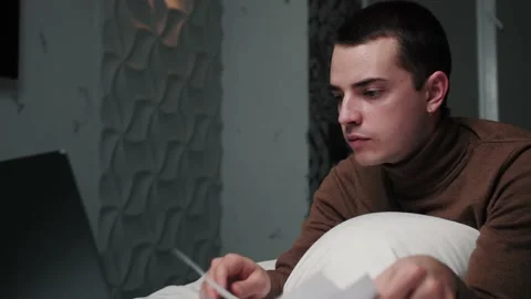 Man with paper documents working on Laptop on Bed. Tired man working at home 스톡 동영상 144311926