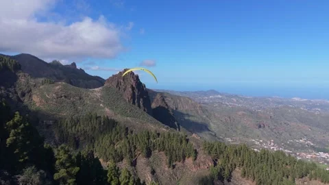 Man on paraglider flies over pine forest and approaches rock formation called 스톡 동영상 298121668