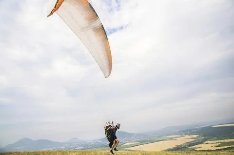 A man paraglider taking off from the edge of the mountain with fields in the Foto stock