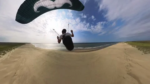 Man paragliding over sandy beach with ocean views, clear sky, and wide Vídeos de archivo 283108264