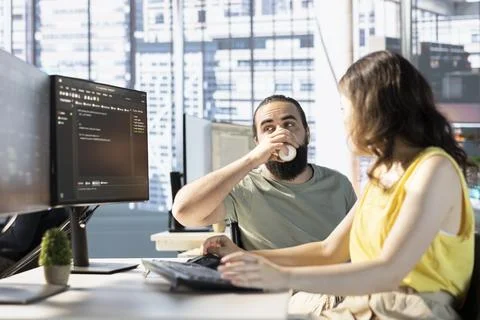 Man with paraplegia drinking coffee, checking colleague doing code review 写真素材