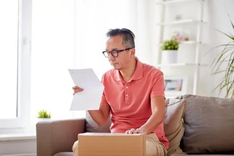 Man with parcel box reading invoice at home Foto stock