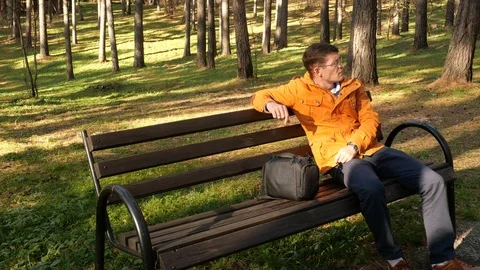 A man in the park sitting on a bench. Stock Footage 118285929
