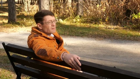 A man in the park sitting on a bench. Stock Footage 118285940