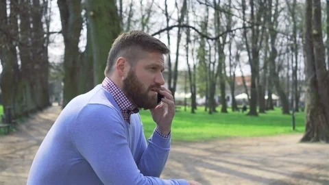 Man in park, talking by smartphone, profile steadycam shot 库存影片 74228231