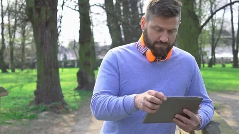 Man in park, typing message on tablet, smile at camera, portrait, steadicam shot Vidéo 74233322