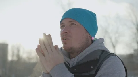 A man in the park in the winter warms his hands, breathes on them and rubs Stock Footage 102281315
