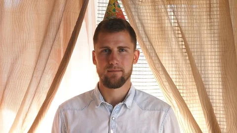 A man in a party hat blows out candle on cupcake Stock Footage 80603659
