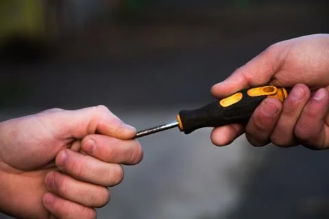 A man passes a screwdriver to another man Stock Photos
