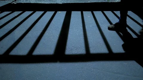 A man passing by the shadow of the grate on the asphalt dark city street Stock Footage 96312863