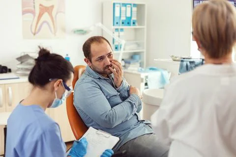 Man patient with tooth pain explaining dental problem to nurse Stock Photos