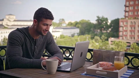 Man on patio having coffee watching content on computer Stock Footage 298029140