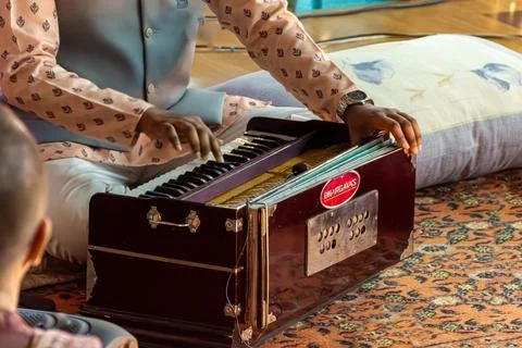 Man in patterned shirt playing dark wooden harmonium with BHARGAVAS logo Stock Photos
