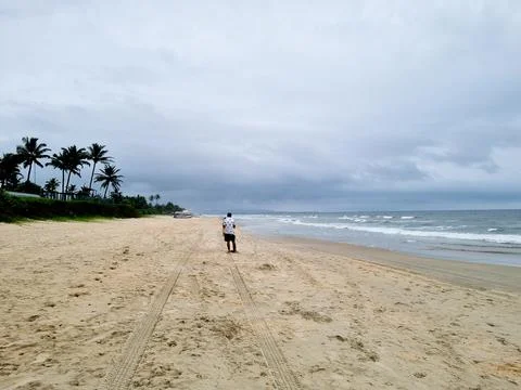 Man in patterned shirt standing on an empty beach with monsoon clouds waves on Stock Photos