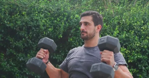 Man pausing, grabbing black hex dumbbells, pressing overhead for strength in Stock Footage 335575290